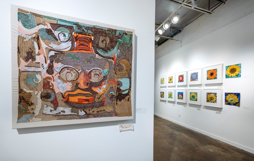 Art gallery with a large mosaic artwork on a wall and smaller paintings on another wall.